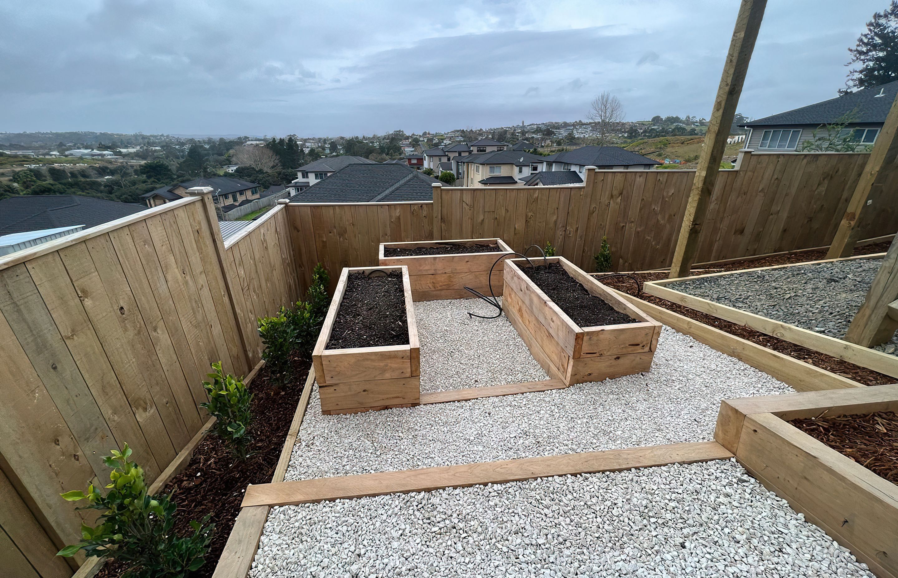 Three newly built vegetable beds raised off the ground in wood casings, surrounded by a white pebble walkway