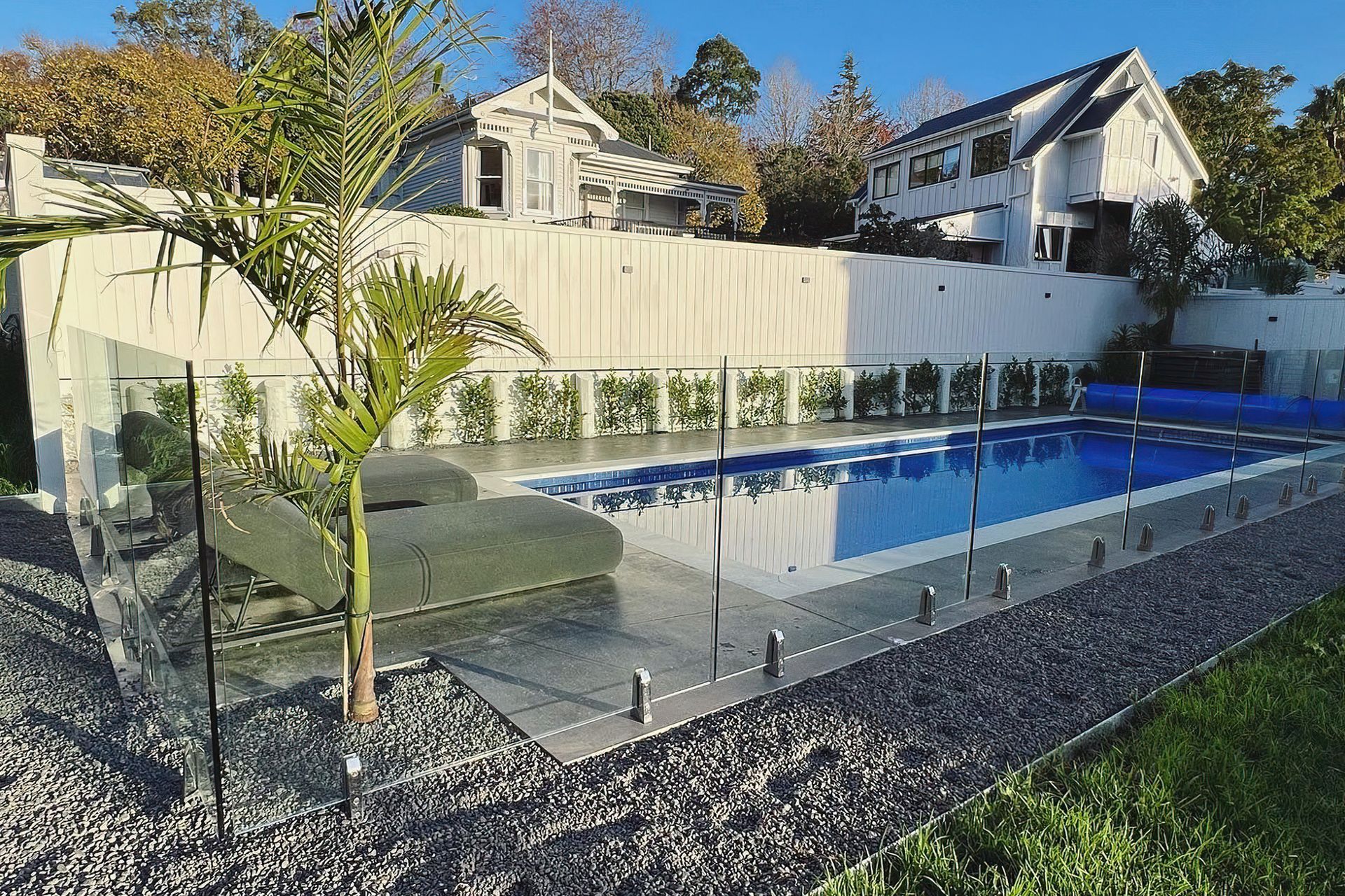 Small to medium sized pool with a concrete path surrounded by gravel and divided by a modern glass fence