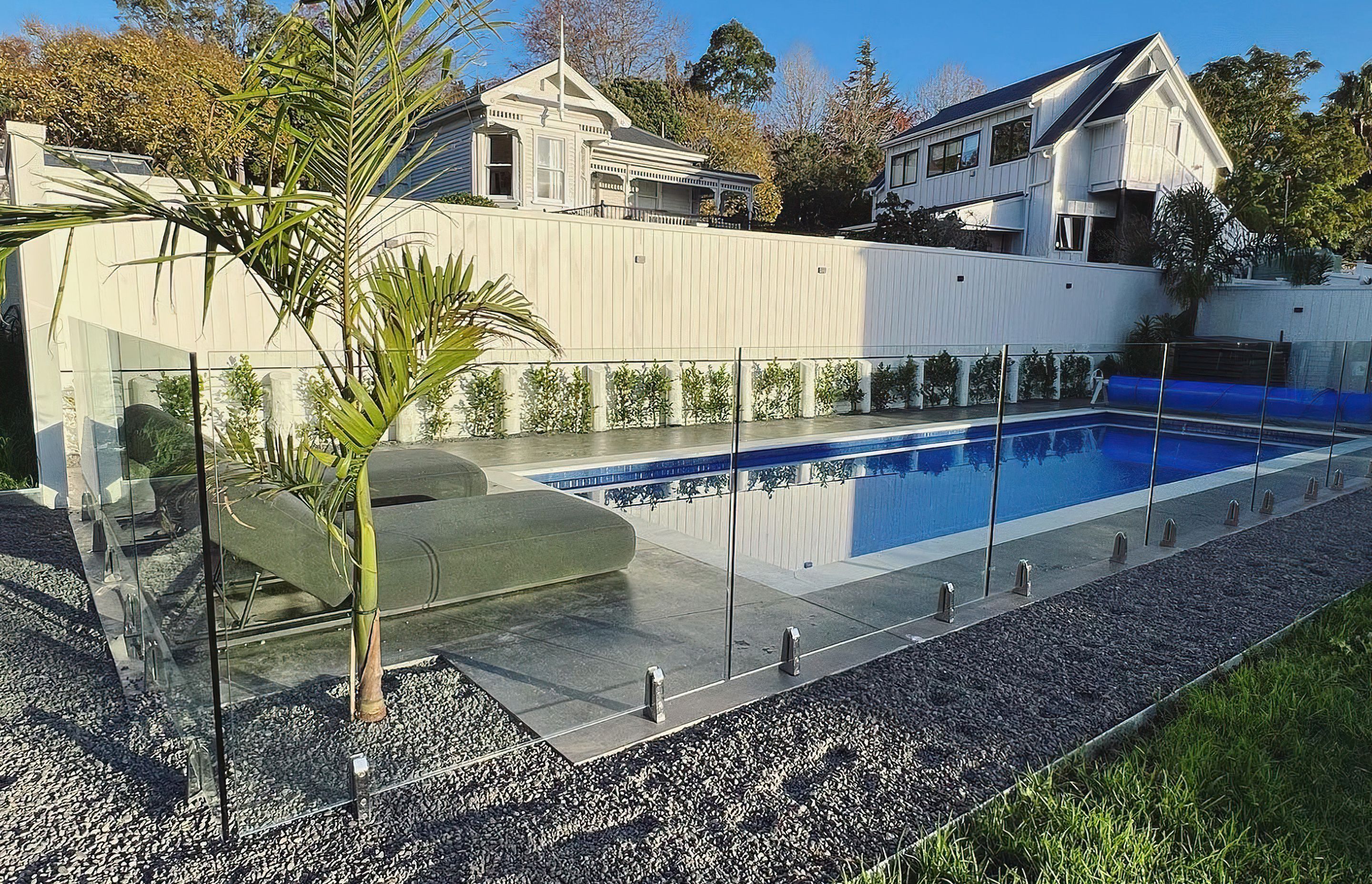 Small to medium sized pool with a concrete path surrounded by gravel and divided by a modern glass fence