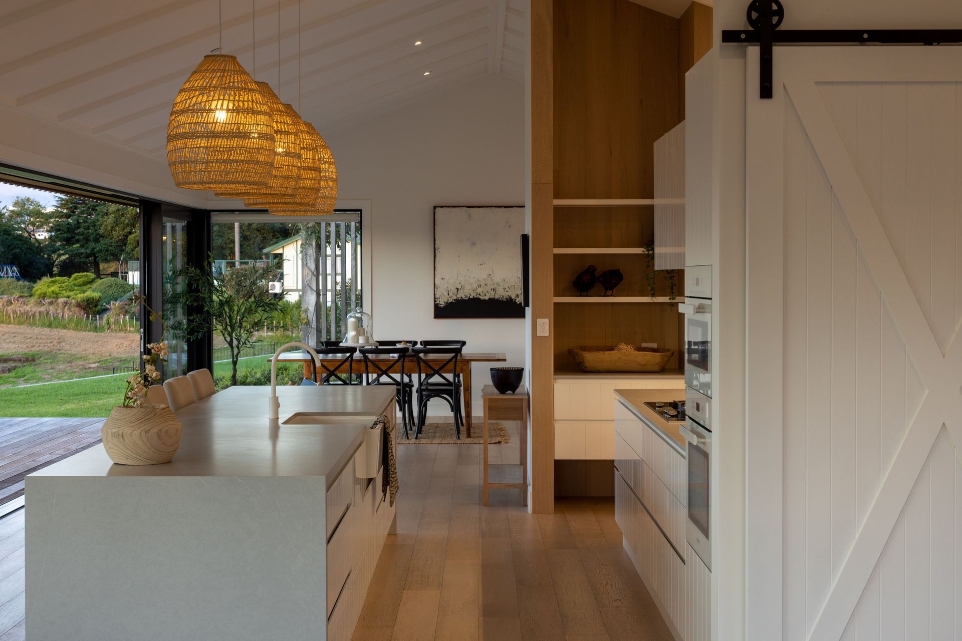 A close-up of the kitchen reveals pale stone surfaces juxtaposed against blonded timber and rustic rattan.