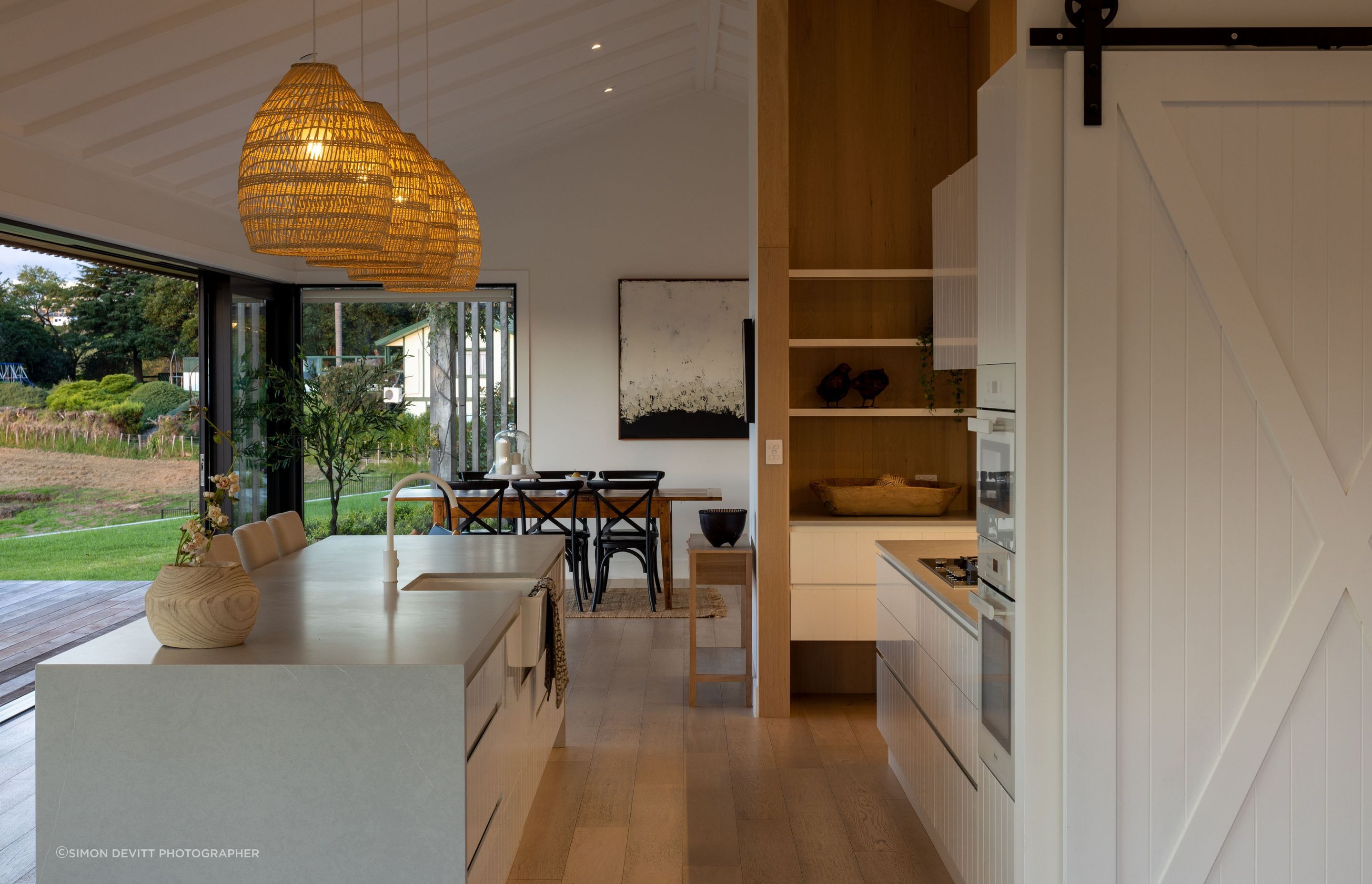 A close-up of the kitchen reveals pale stone surfaces juxtaposed against blonded timber and rustic rattan.