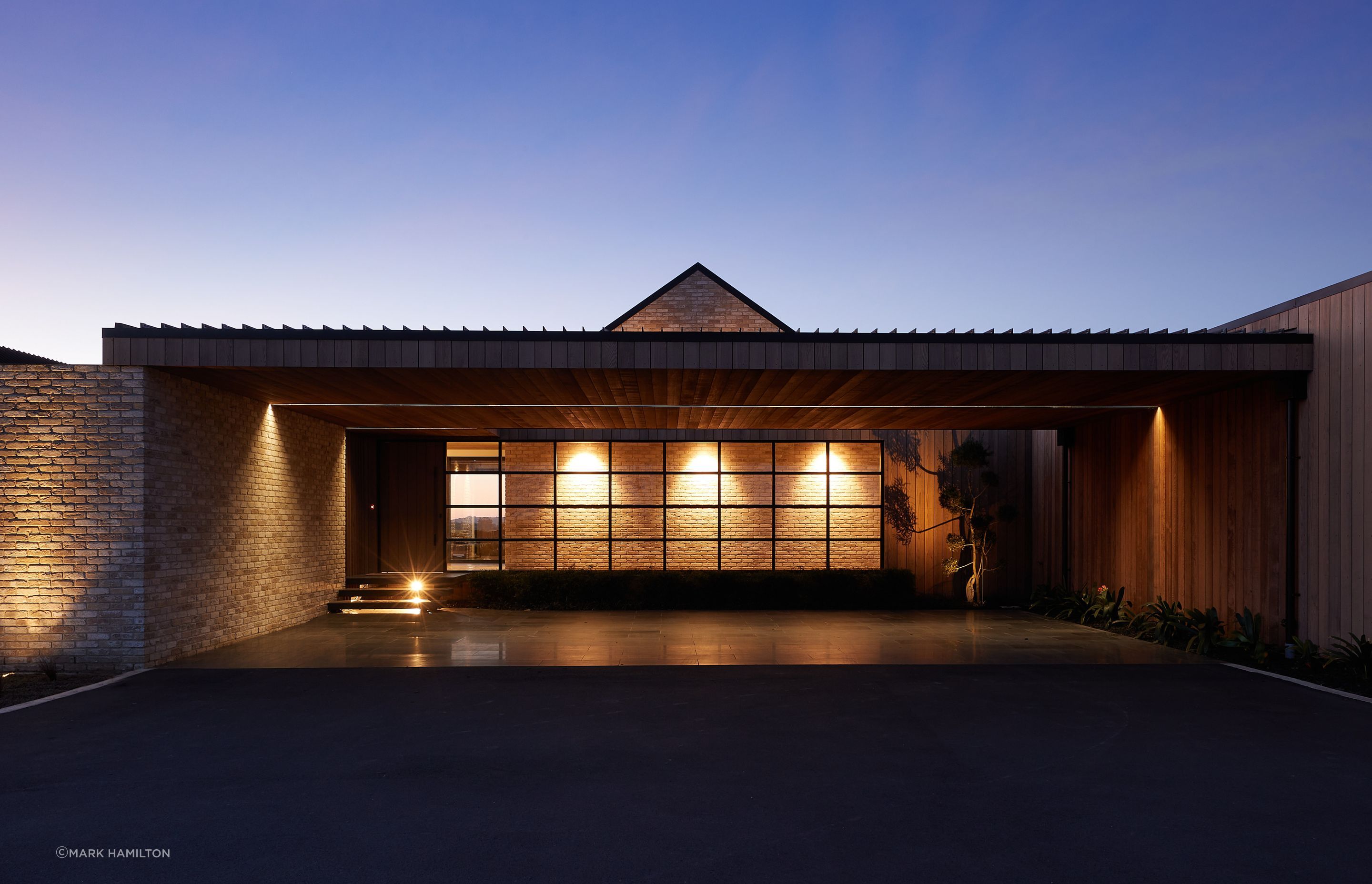 The entry to the home features a sheltered brick pavilion with a glazed wall that allows you to see the form of the gabled living room space within.