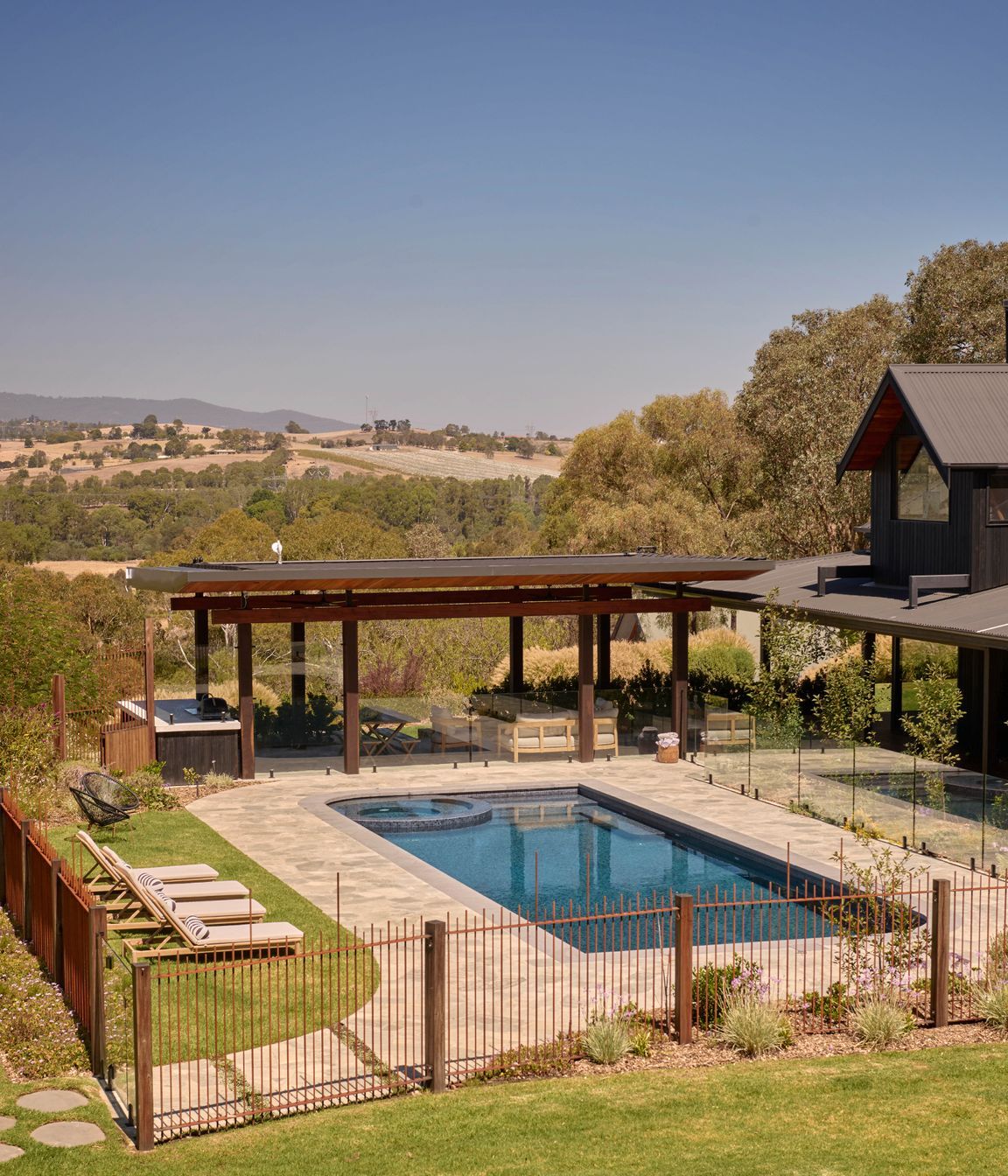 Endicott paving by Eco Outdoor around pool. Custom concrete barbecue area bench with charred timber cladding from Eco Timber Group. Sun loungers from Temple & Webster. The property looks out to Croydon and Lilydale in the distance. Pool designed with Living Landscapes Design and constructed by Saltwater Pools.