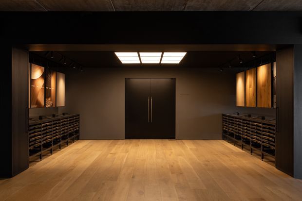 Dark, refined wine cellar with symmetrical built-in wine storage racks along both side walls, warm timber flooring, dark cabinetry and double doors, timber display niches, and a central rectangular ceiling light.
