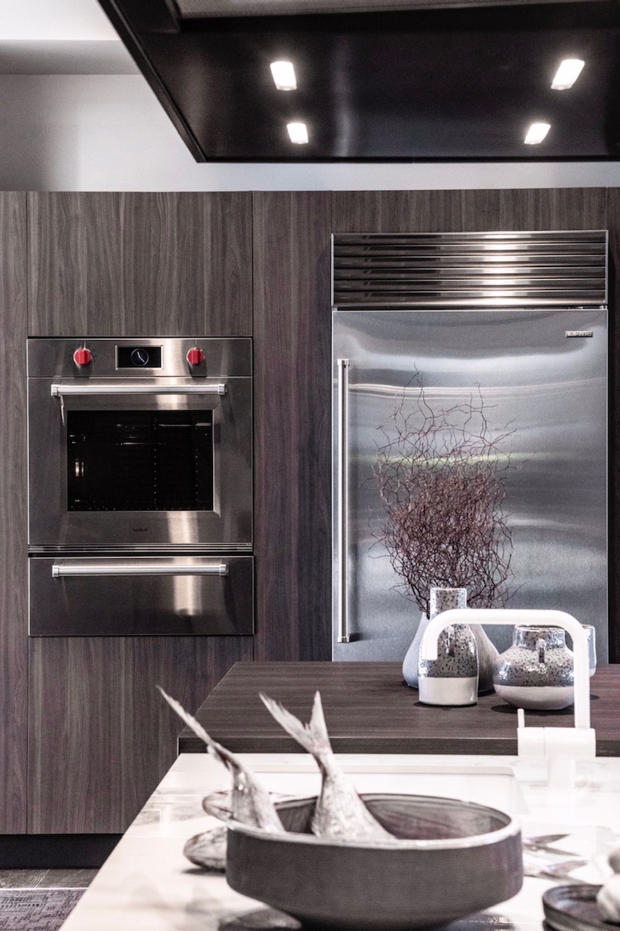 A Qasair custom rangehood hangs over a classic marble island. Sub-Zero and Wolf appliances are shown in this display by Unico.