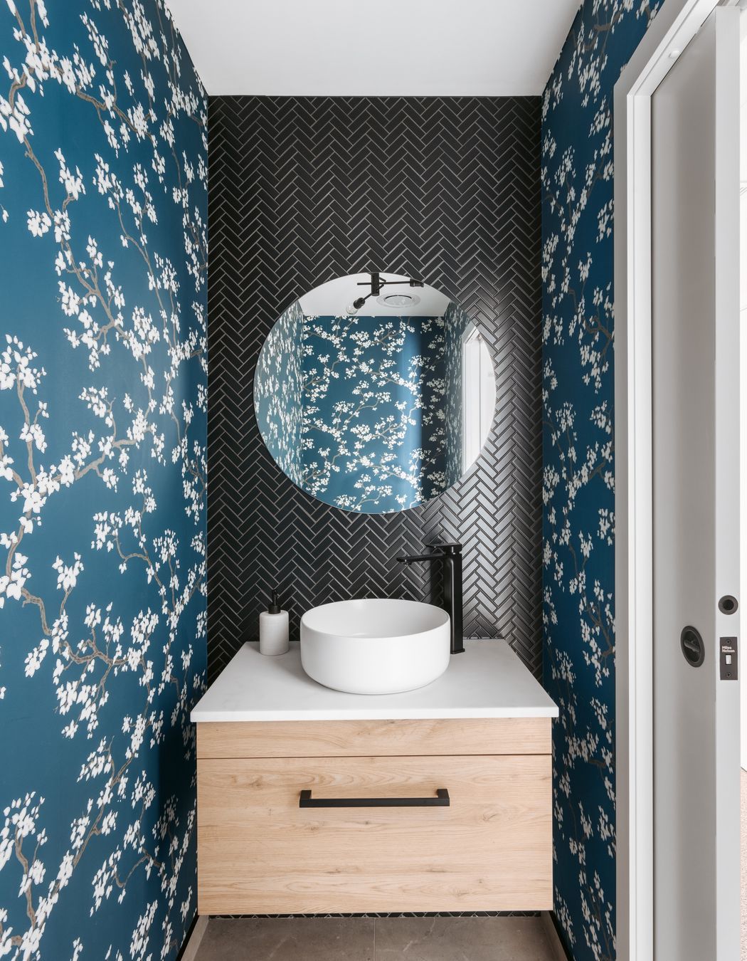 The guest powder room delights with its black herringbone tiles and cherry blossom covered wallpaper.