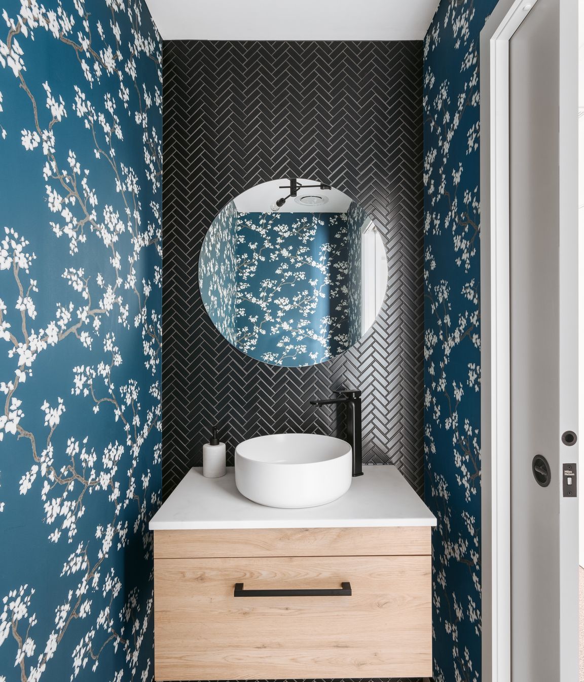 The guest powder room delights with its black herringbone tiles and cherry blossom covered wallpaper.