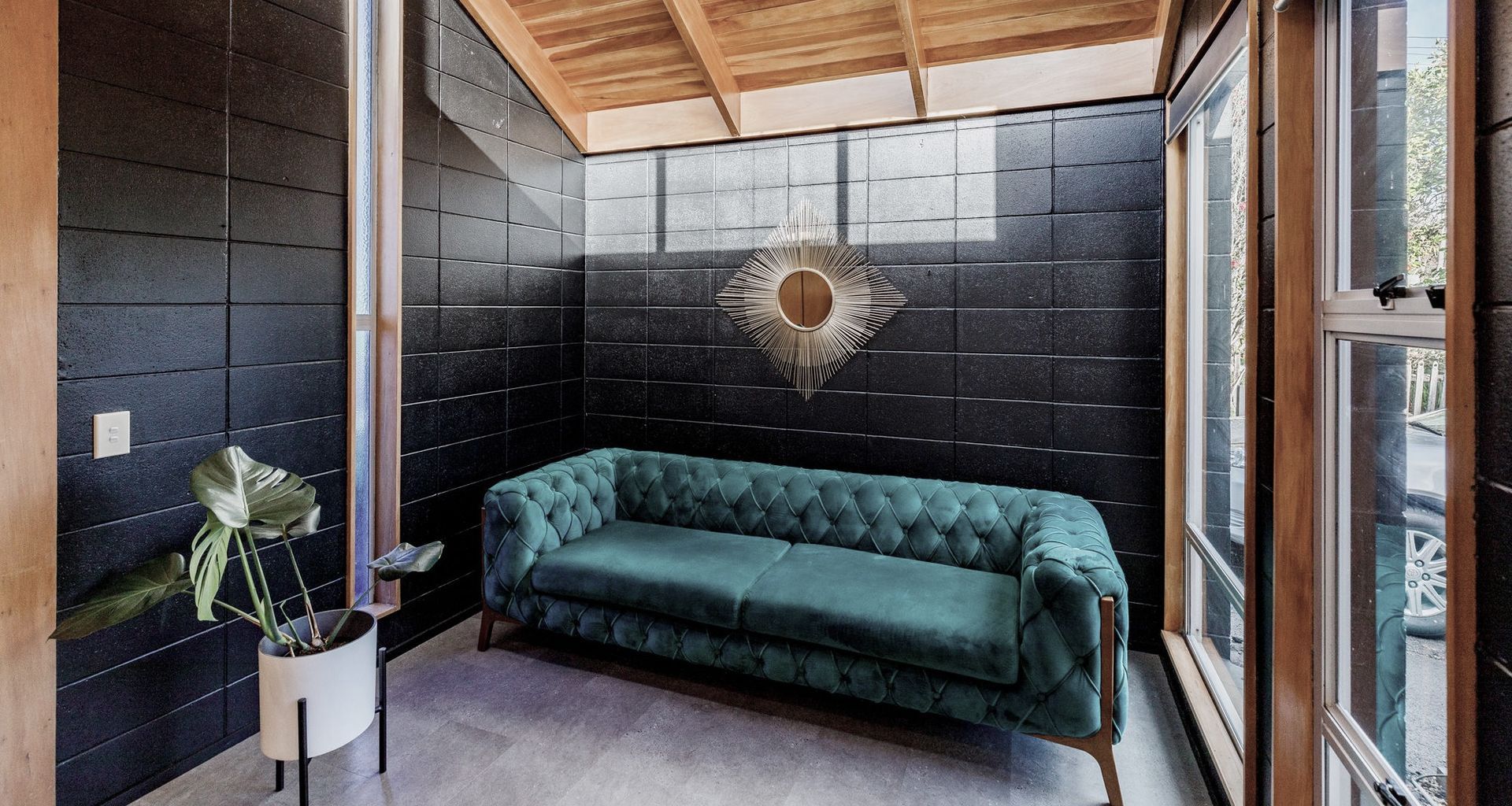 Bathed in sunlight from high windows, the Sitting Room exudes warmth and character. The exposed timber ceiling beautifully offsets the sleek black painted concrete block walls, which create a striking contrast against the prevailing wood in this open-plan space.
