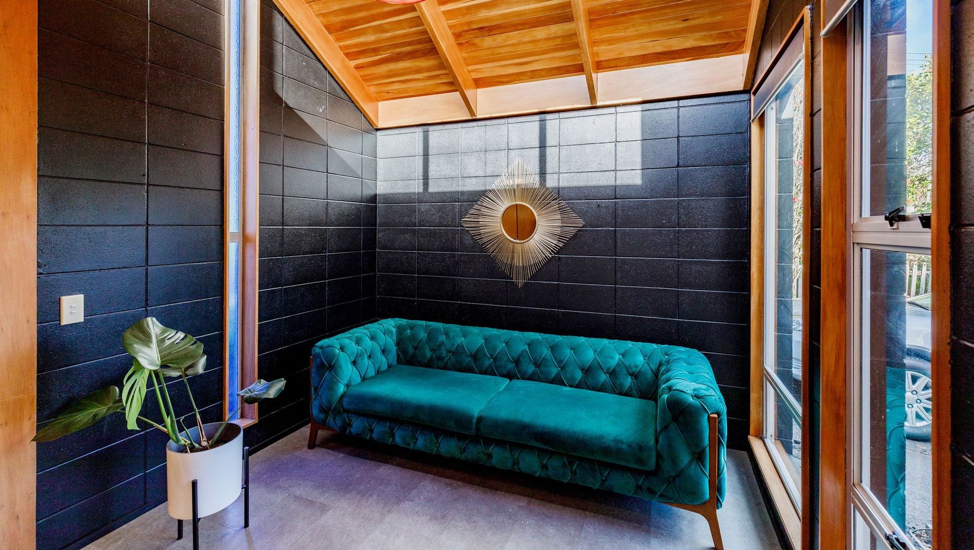 Bathed in sunlight from high windows, the Sitting Room exudes warmth and character. The exposed timber ceiling beautifully offsets the sleek black painted concrete block walls, which create a striking contrast against the prevailing wood in this open-plan space.