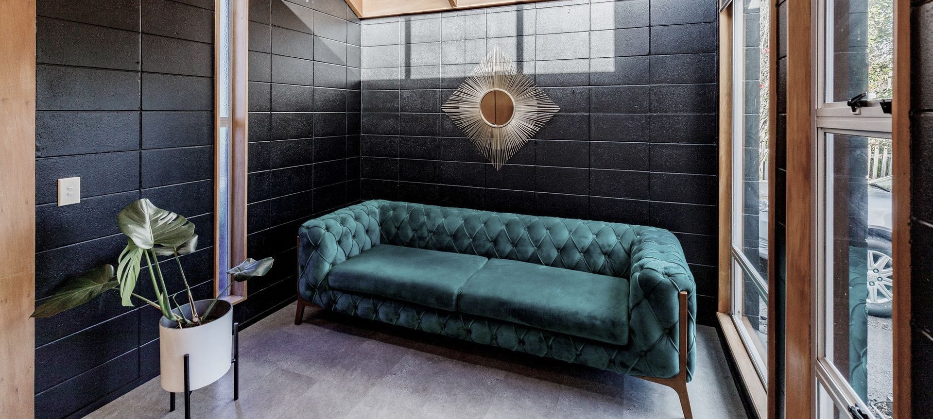 Bathed in sunlight from high windows, the Sitting Room exudes warmth and character. The exposed timber ceiling beautifully offsets the sleek black painted concrete block walls, which create a striking contrast against the prevailing wood in this open-plan space.