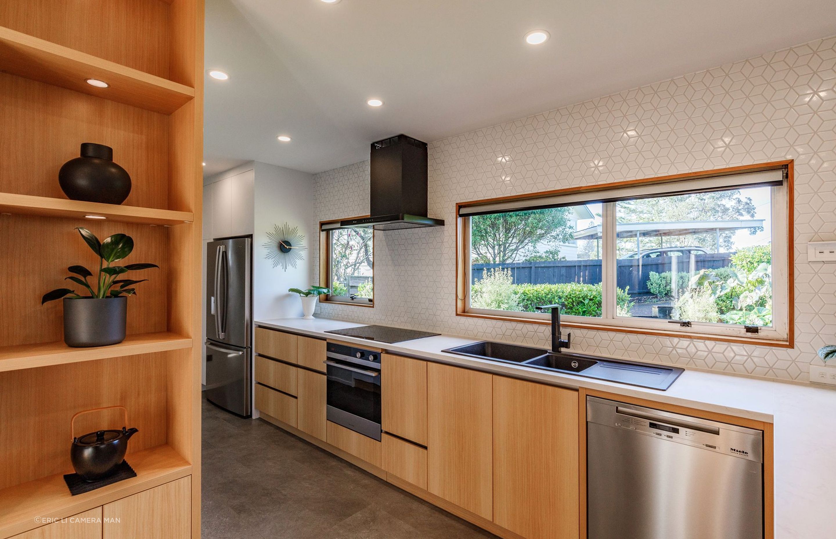 The blend of wood, white, and black accents creates a timeless and inviting ambiance, while the textured splashback tiles add subtle interest.