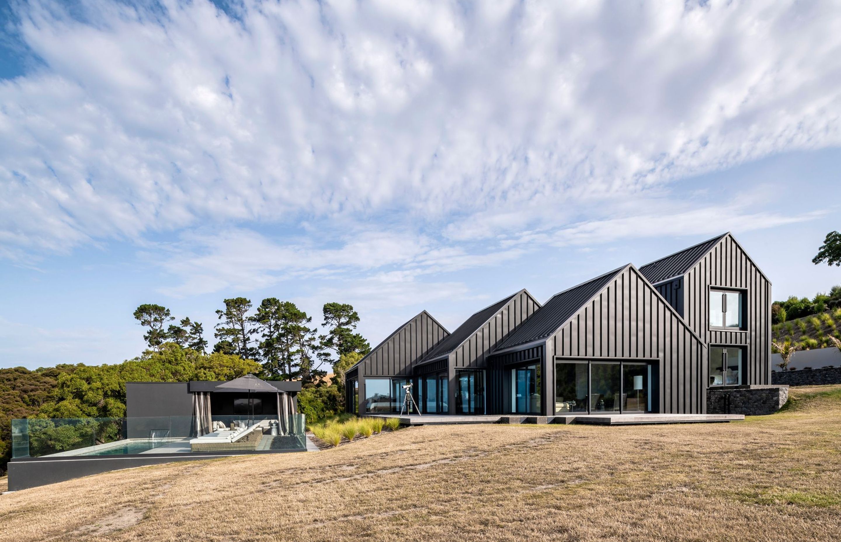 The home with its five striking gable forms, unfurls in the landscape down to a pool and cabana at the bottom of the slope.