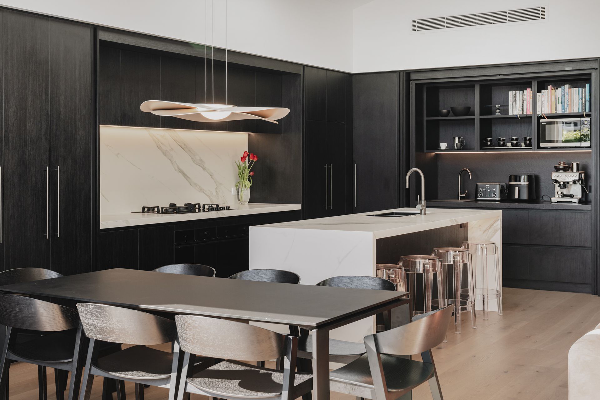 Westmere Bungalow | New-Build Residence | Internal view of dark wood kitchen with marble waterfall island and splashback, with bespoke cabinetry concealing deep pantries and storage.