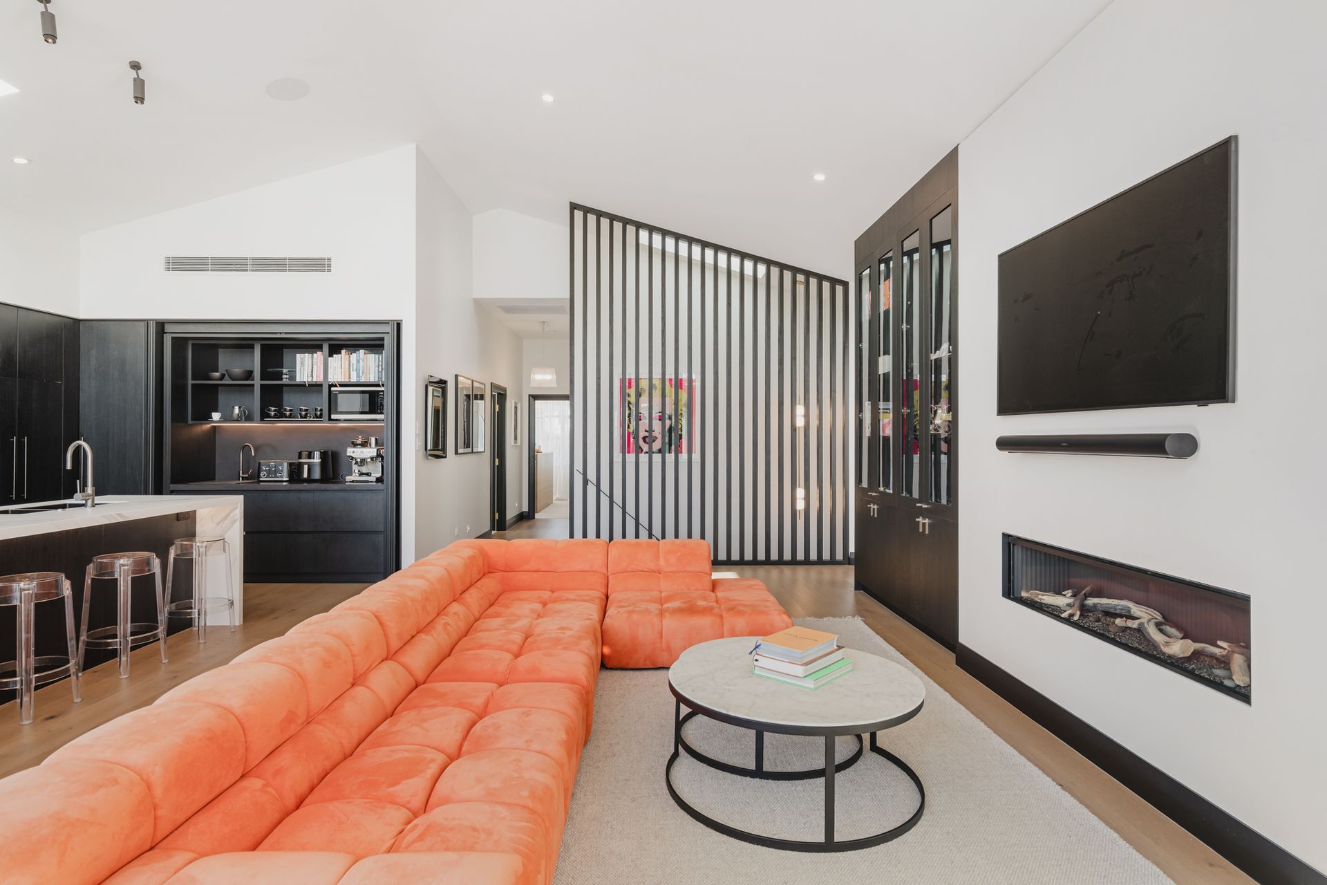 Westmere Bungalow | New-Build Residence | Internal view of open plan living, kitchen and dining room, featuring sweeping high pitch ceilings, gas fireplace and bespoke dark wood kitchen.