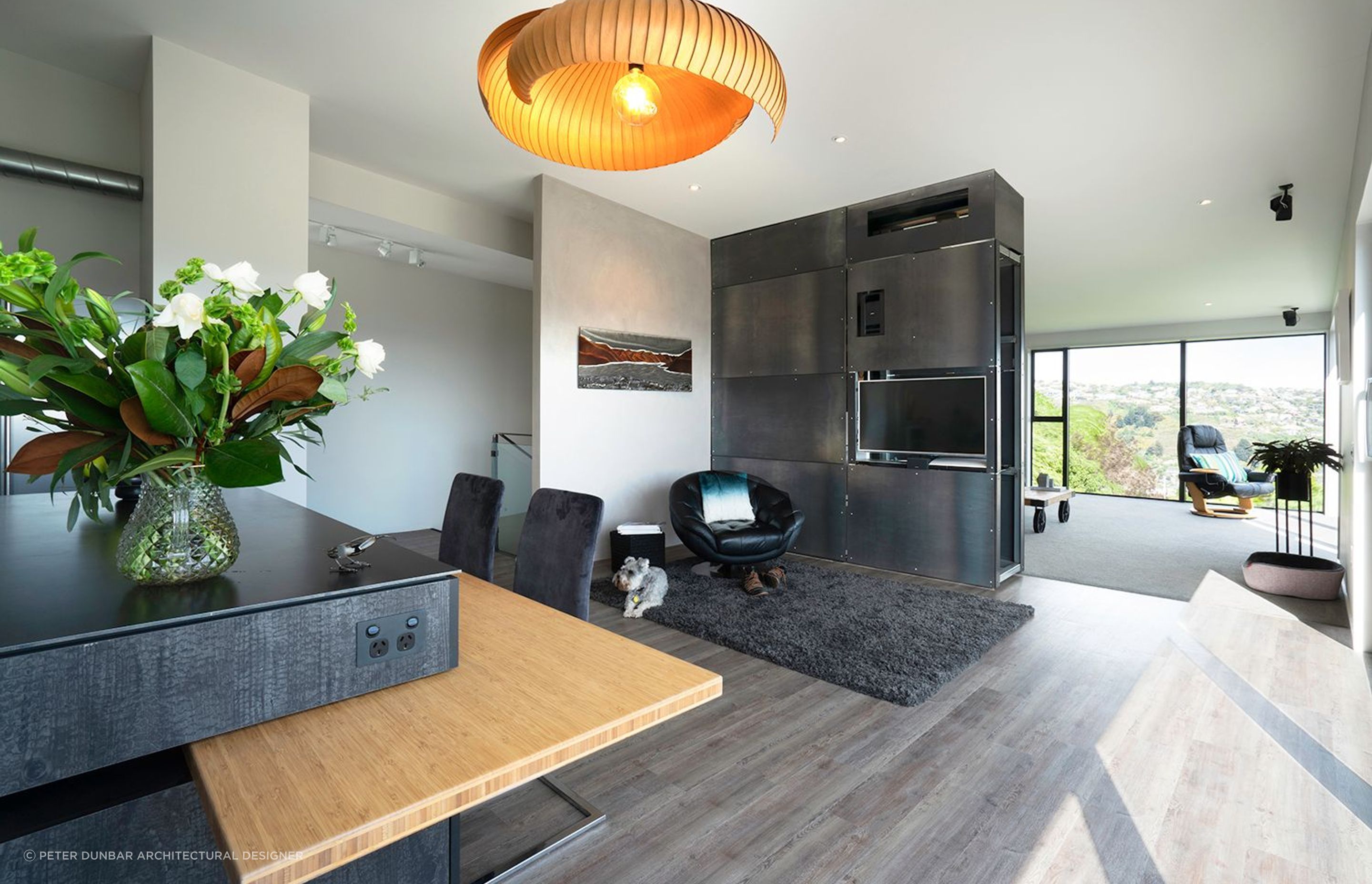 Dining and living area divided by a bespoke design by Peter Dunbar for a pivoting steel wall which includes a TV and air-conditioning unit.