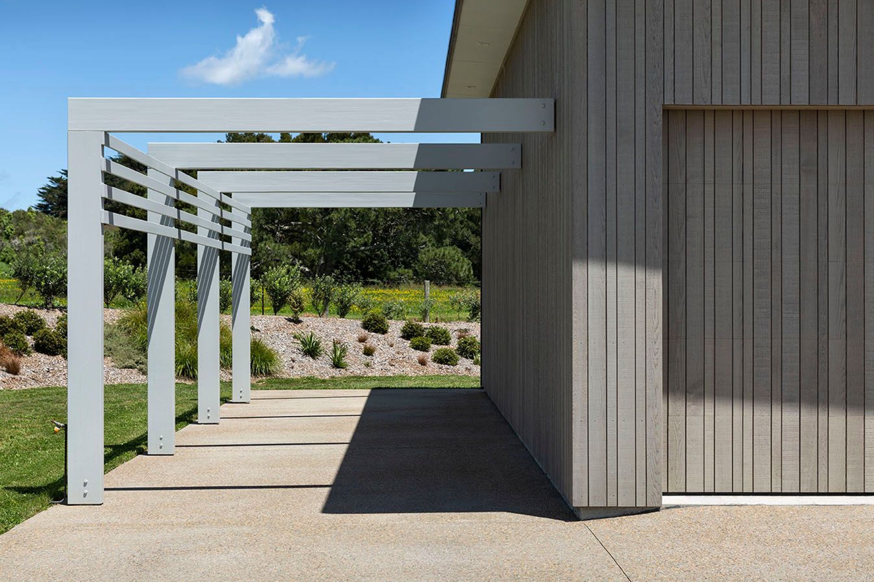 Garage door shares the pattern of the cladding and beautifully sits within the structure while a carport structure adds leading lines and dynamic shadows to the driveway