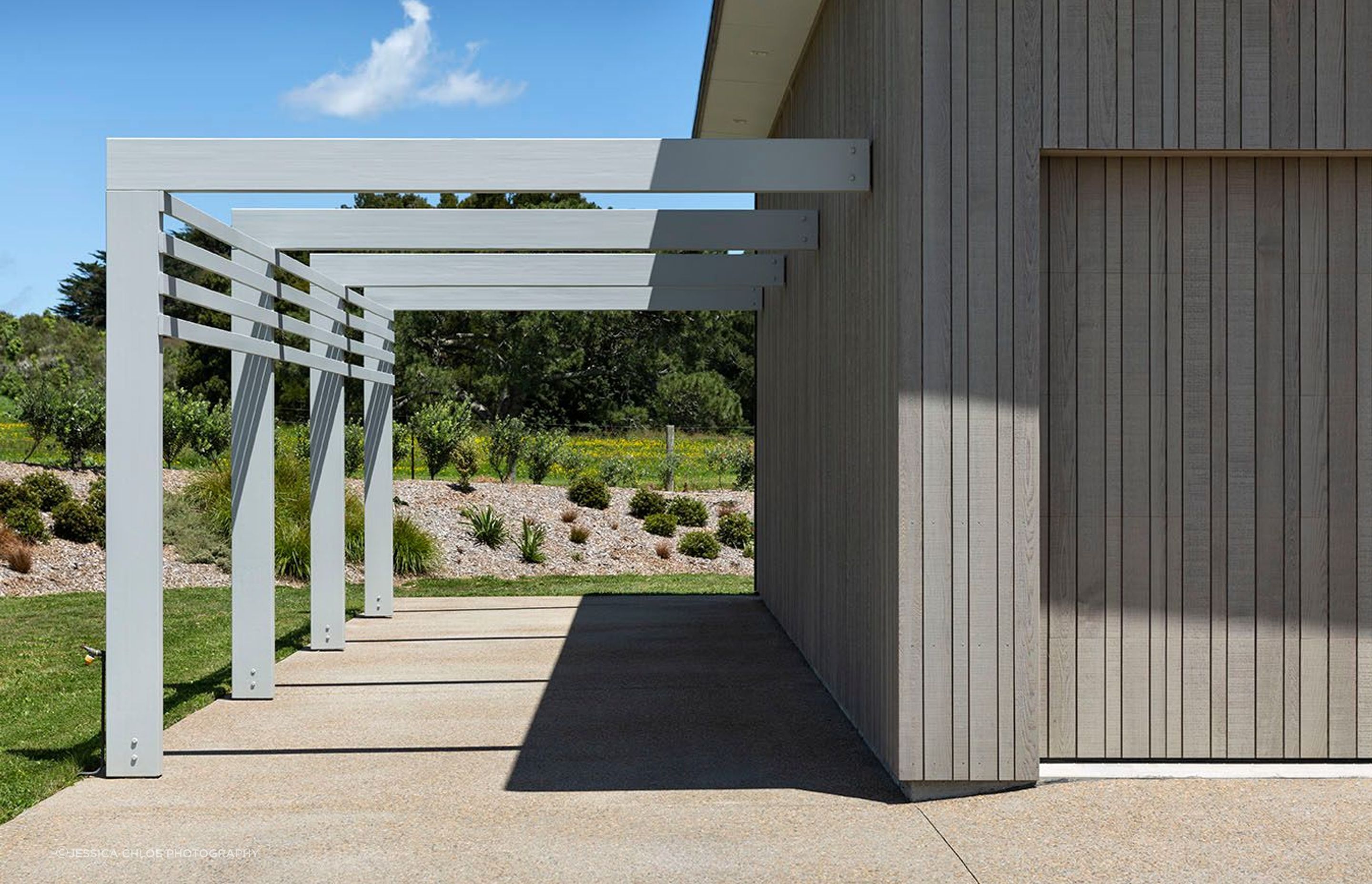 Garage door shares the pattern of the cladding and beautifully sits within the structure while a carport structure adds leading lines and dynamic shadows to the driveway