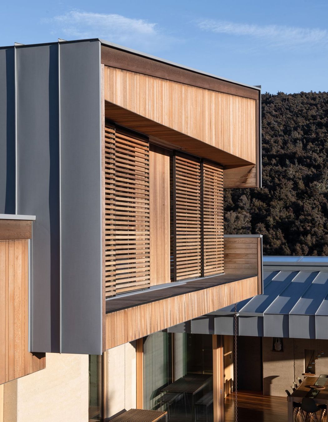 The exterior material palette comprises rammed earth, timber and zinc-coated aluminium.