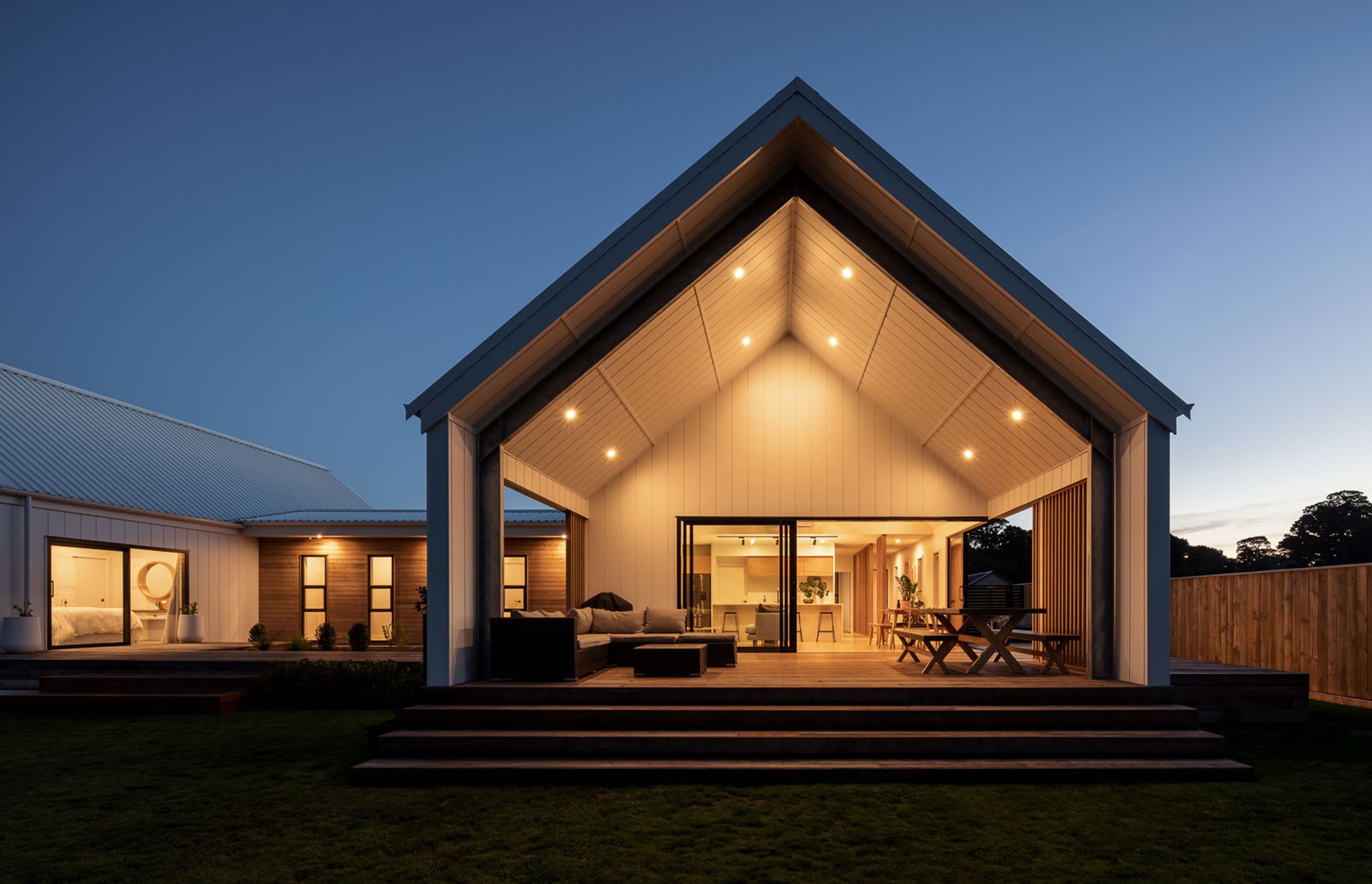 A large stacking slider, along with a level threshold, dissolves the division between inside and the covered living space that terraces down to the lawn and is covered with a large gabled void extruded from the main roof.