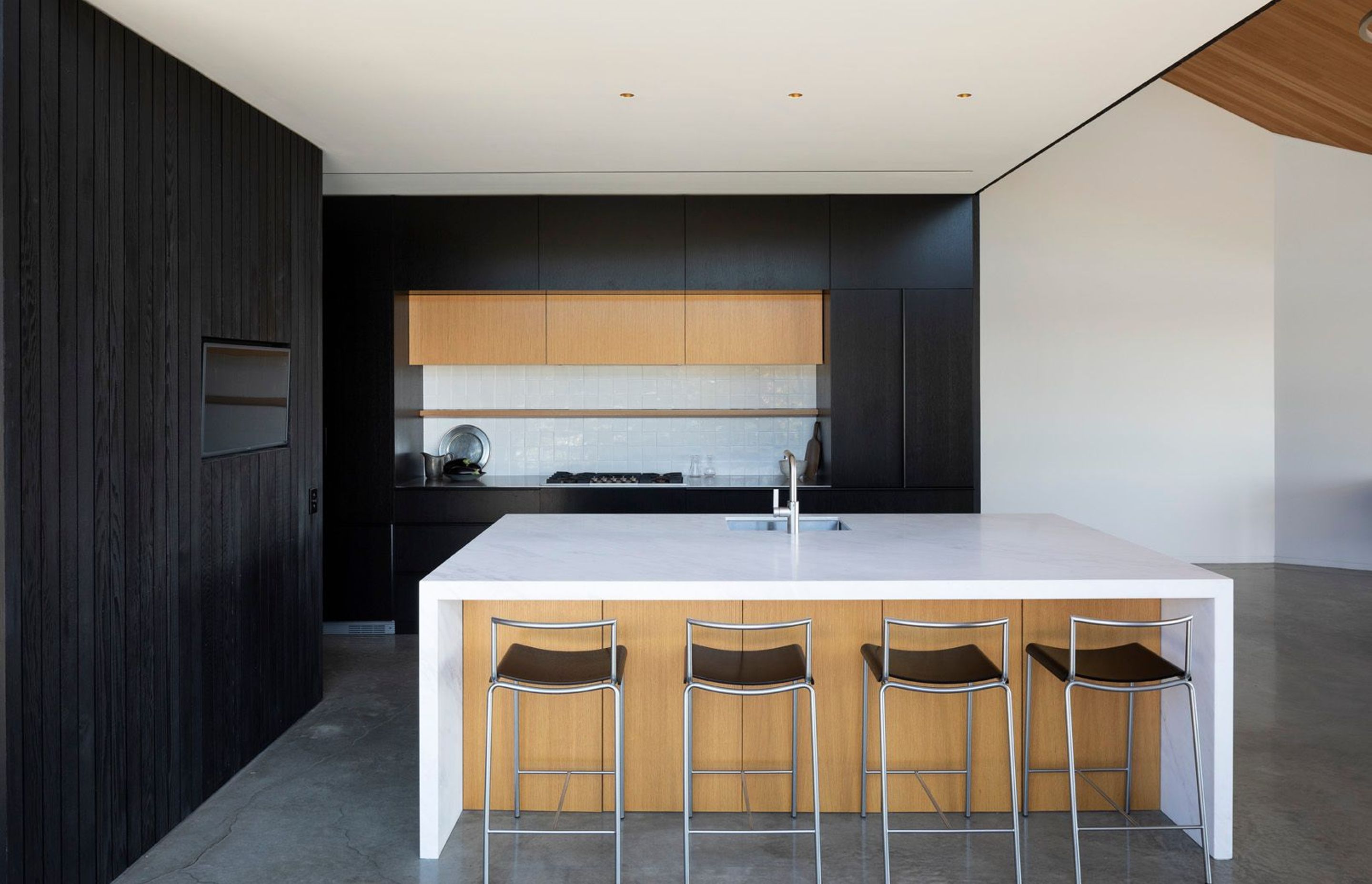 The kitchen is situated under the mezzanine main bedroom, giving this space a more intimate feeling due to the lower ceiling plane. Darkly stained cedar is complemented and contrasted by the other cabinetry and large island.