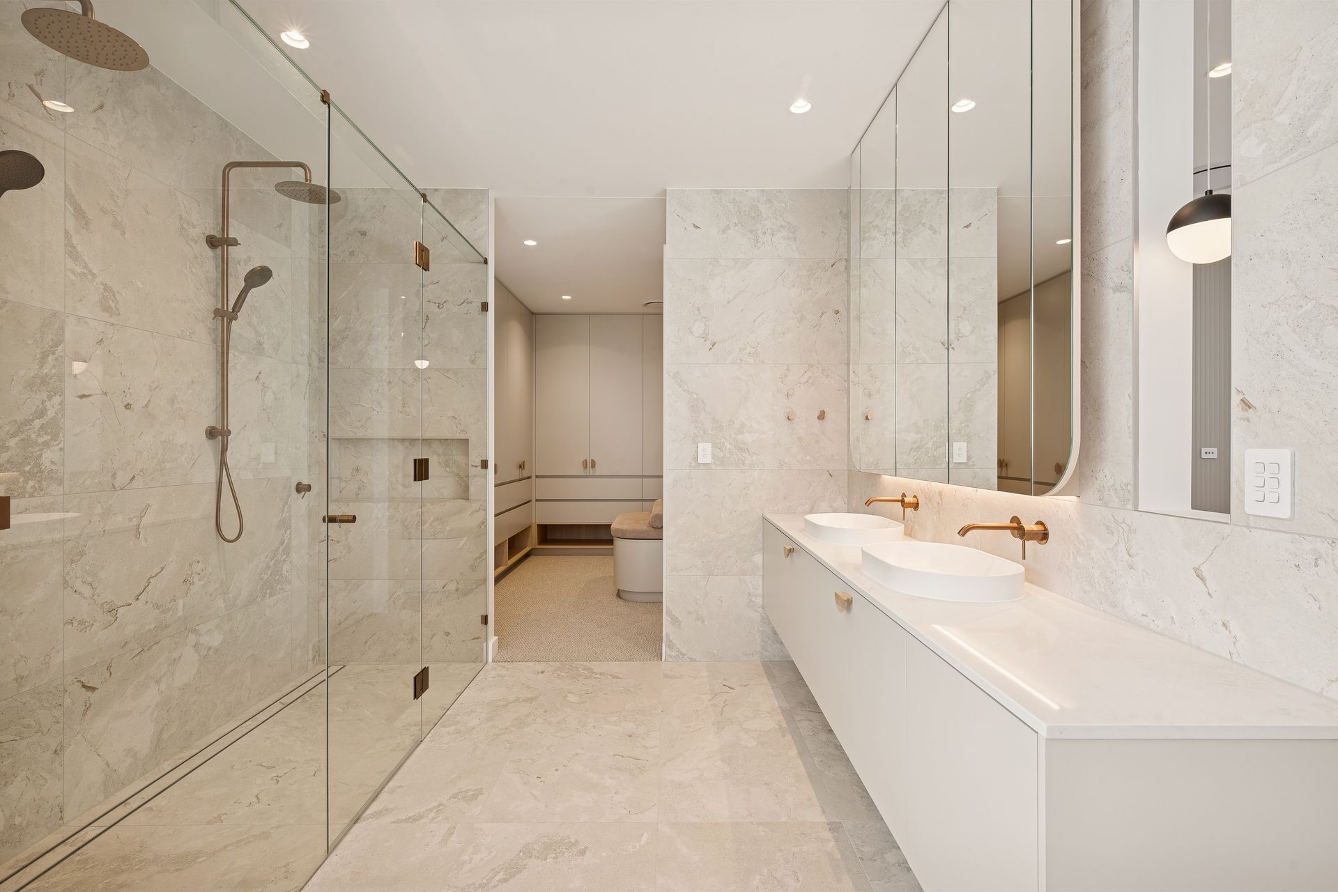 Brass tapware and marble-look tiling meet beneath a pair of pendant lights.