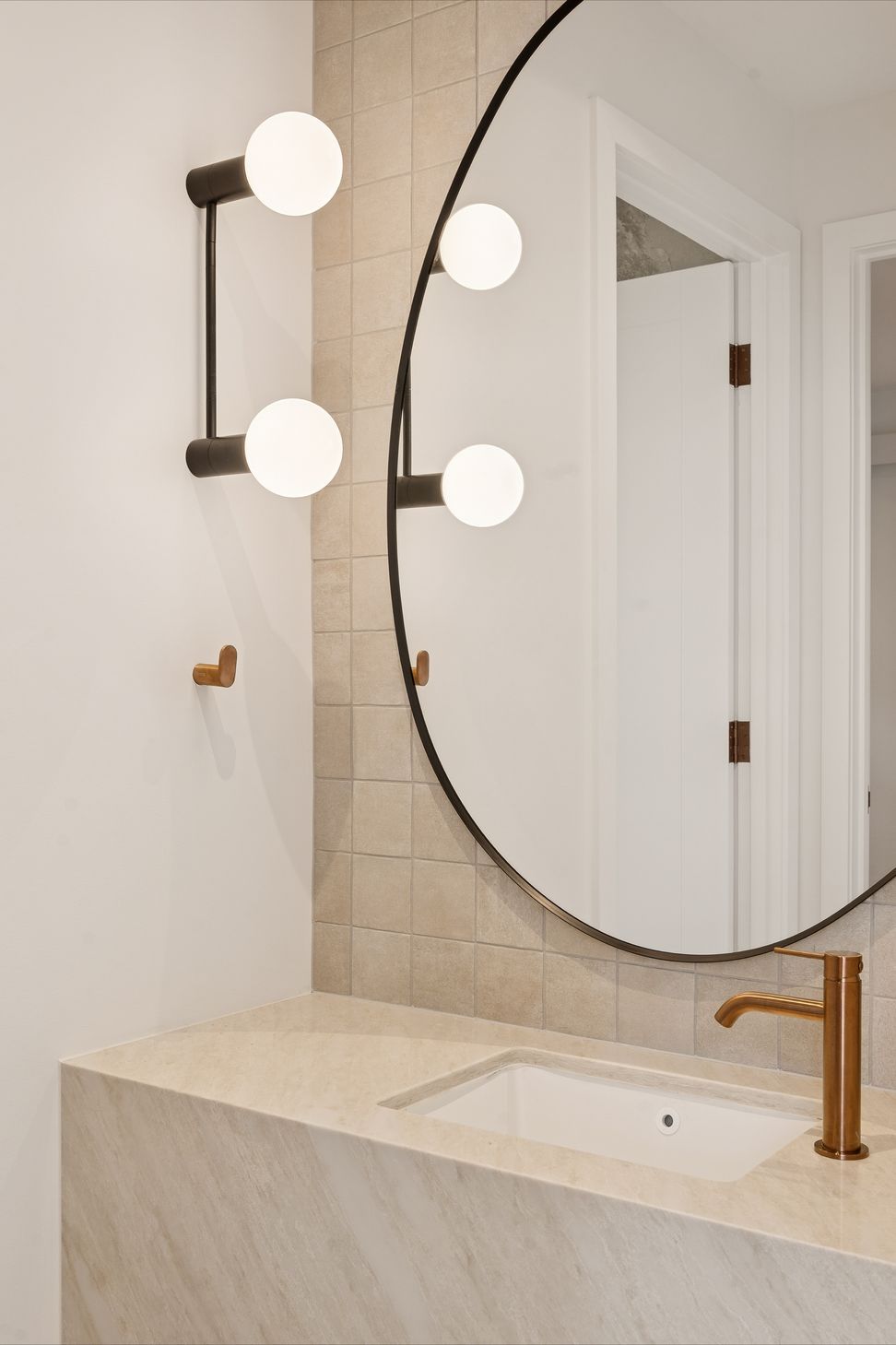 A round wall light and timber-framed mirror keep this powder room warm and simple.