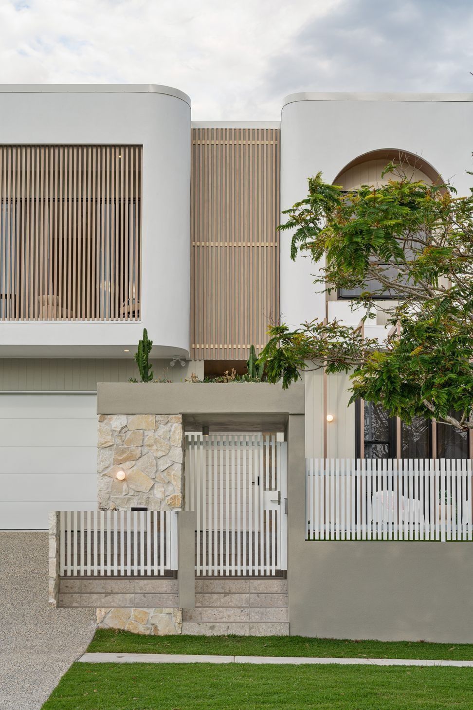 A stone pier and timber battens mark the entry, softened by low garden planting.