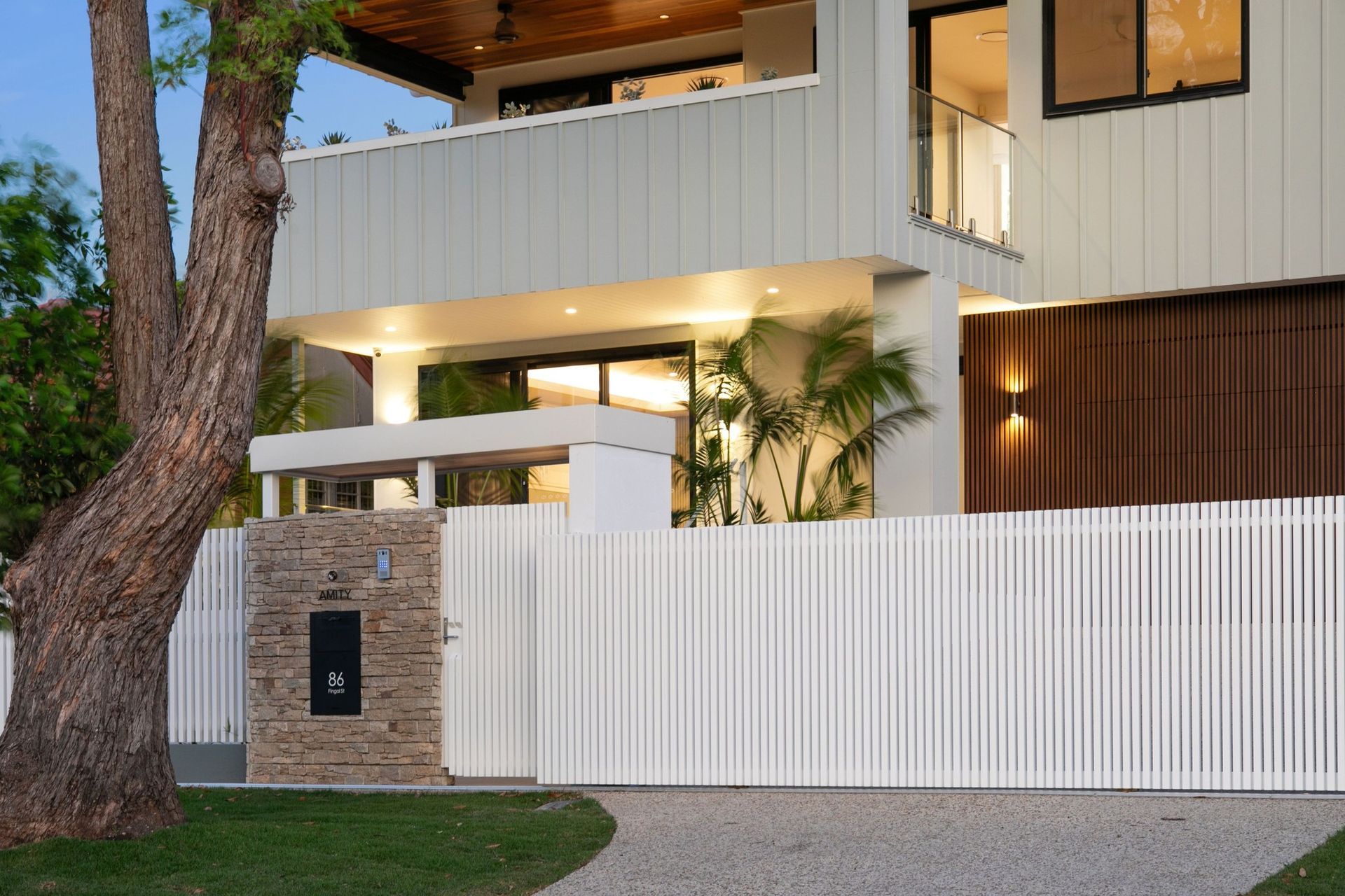 Evening lighting picks out the layers of the entry — stone, battens and palms.