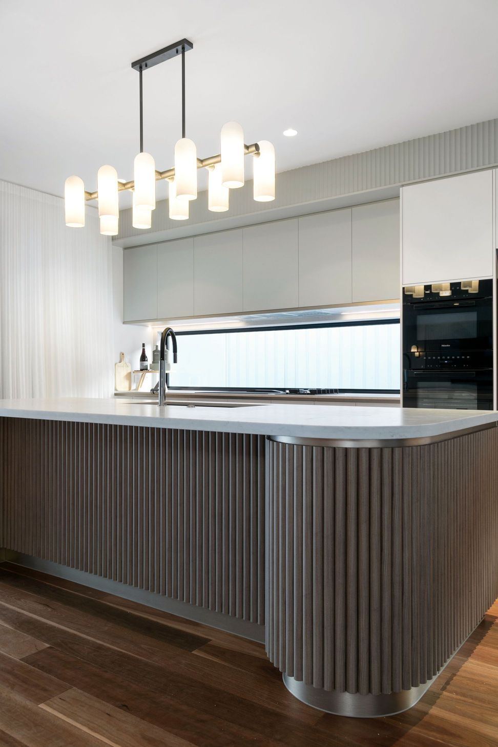 Brass and opal pendants hang low over the island, warming the kitchen's palette after dark.