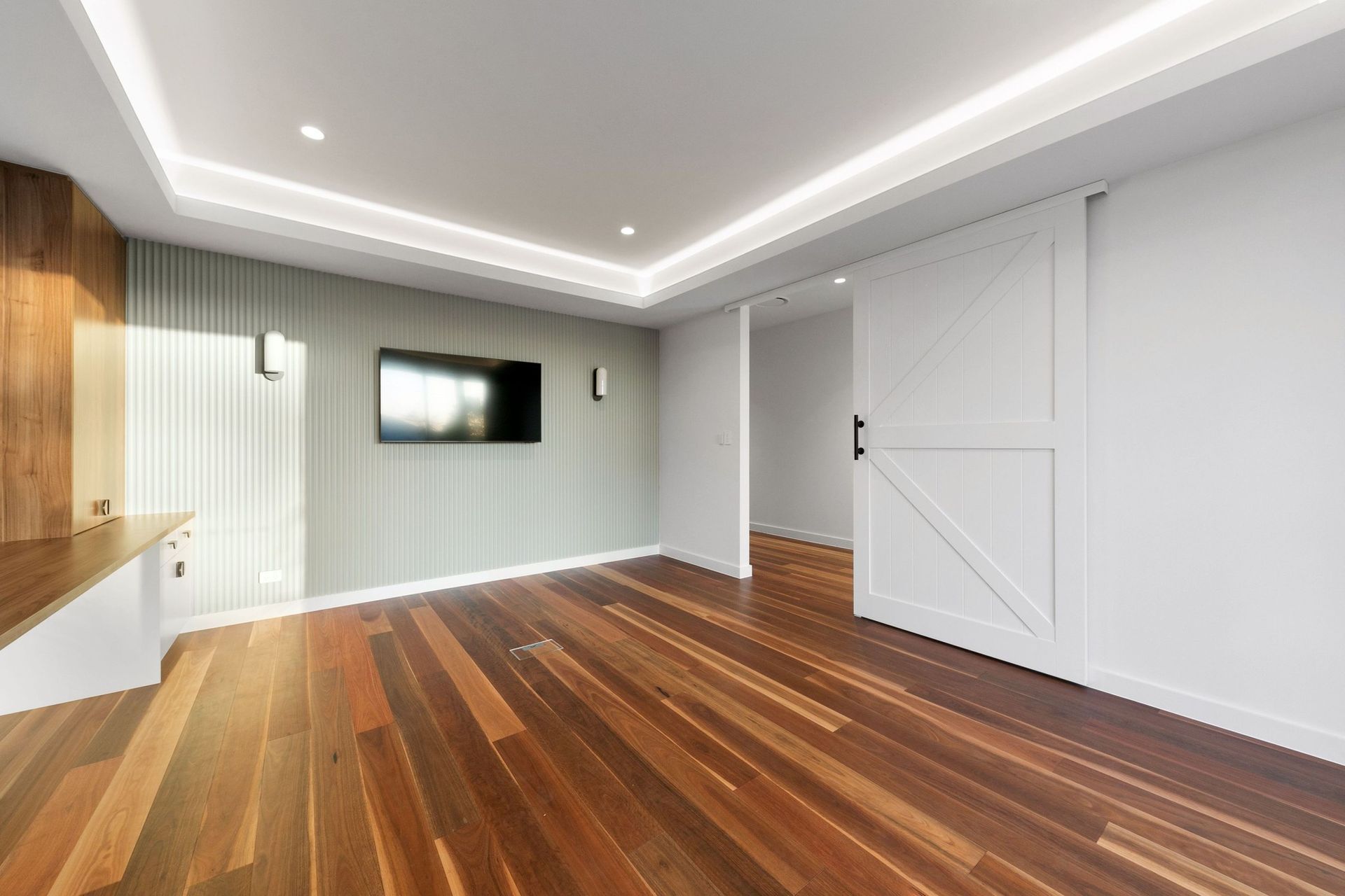 The media room keeps its palette soft — sage fluting and cove lighting over spotted gum.