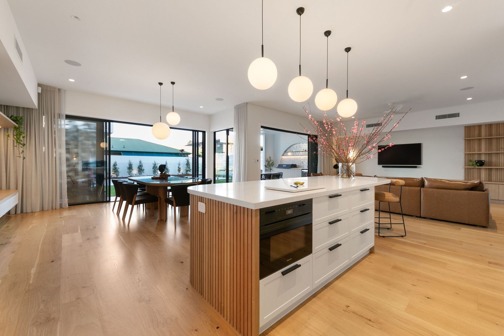 Globe pendants trace the island, with the dining table and pool beyond in one continuous space.