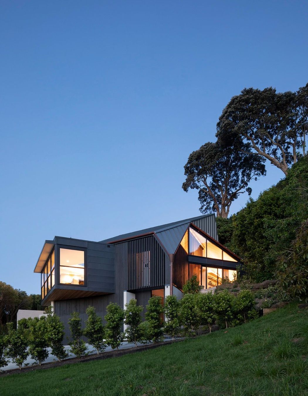 Situated at the end of a 500m driveway, which winds around 12 other houses, the home is perched on the slope of a volcanic crater with views over a wooded dell to the north and Auckland city to the west.