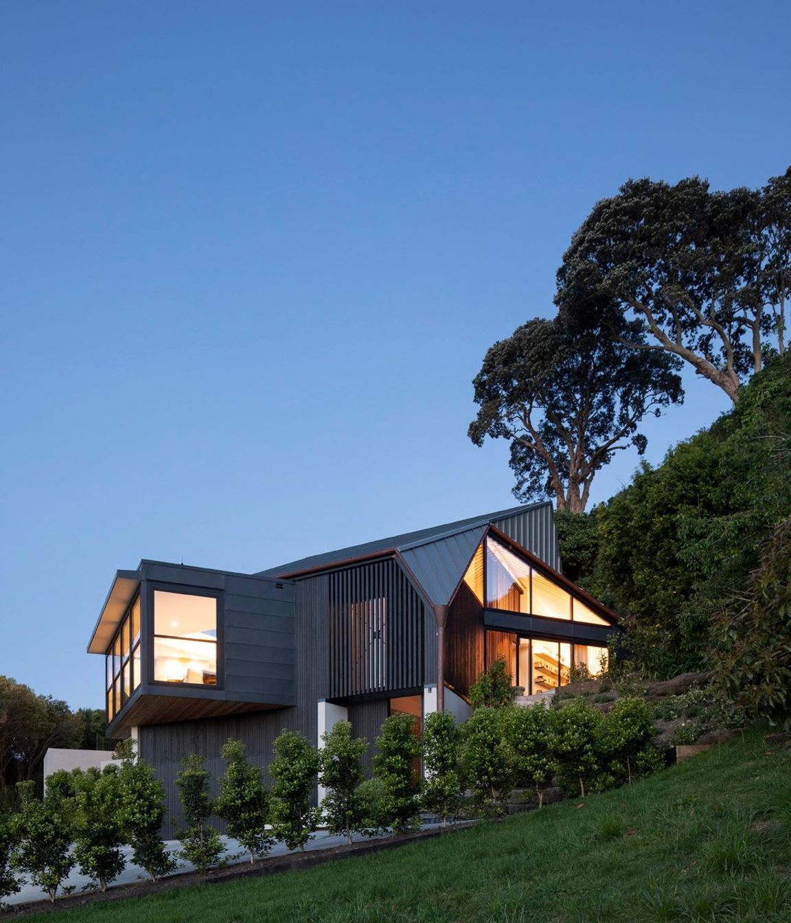 Situated at the end of a 500m driveway, which winds around 12 other houses, the home is perched on the slope of a volcanic crater with views over a wooded dell to the north and Auckland city to the west.