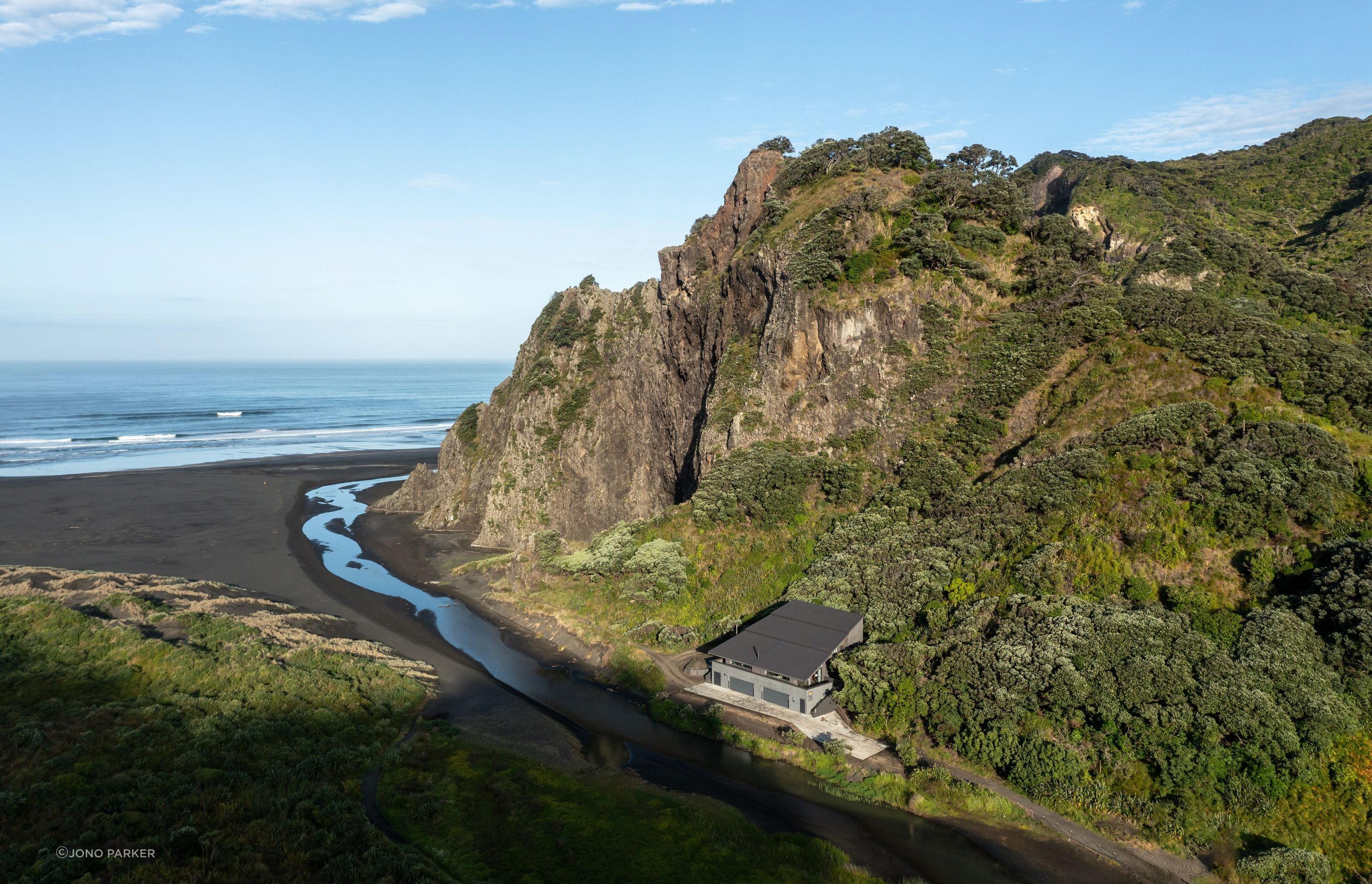 ©️ Jono Parker Nestled into the base of The Watchman basalt cliffs, the Trusts Karekare Surf Life Saving Club takes in the same earthy hues.