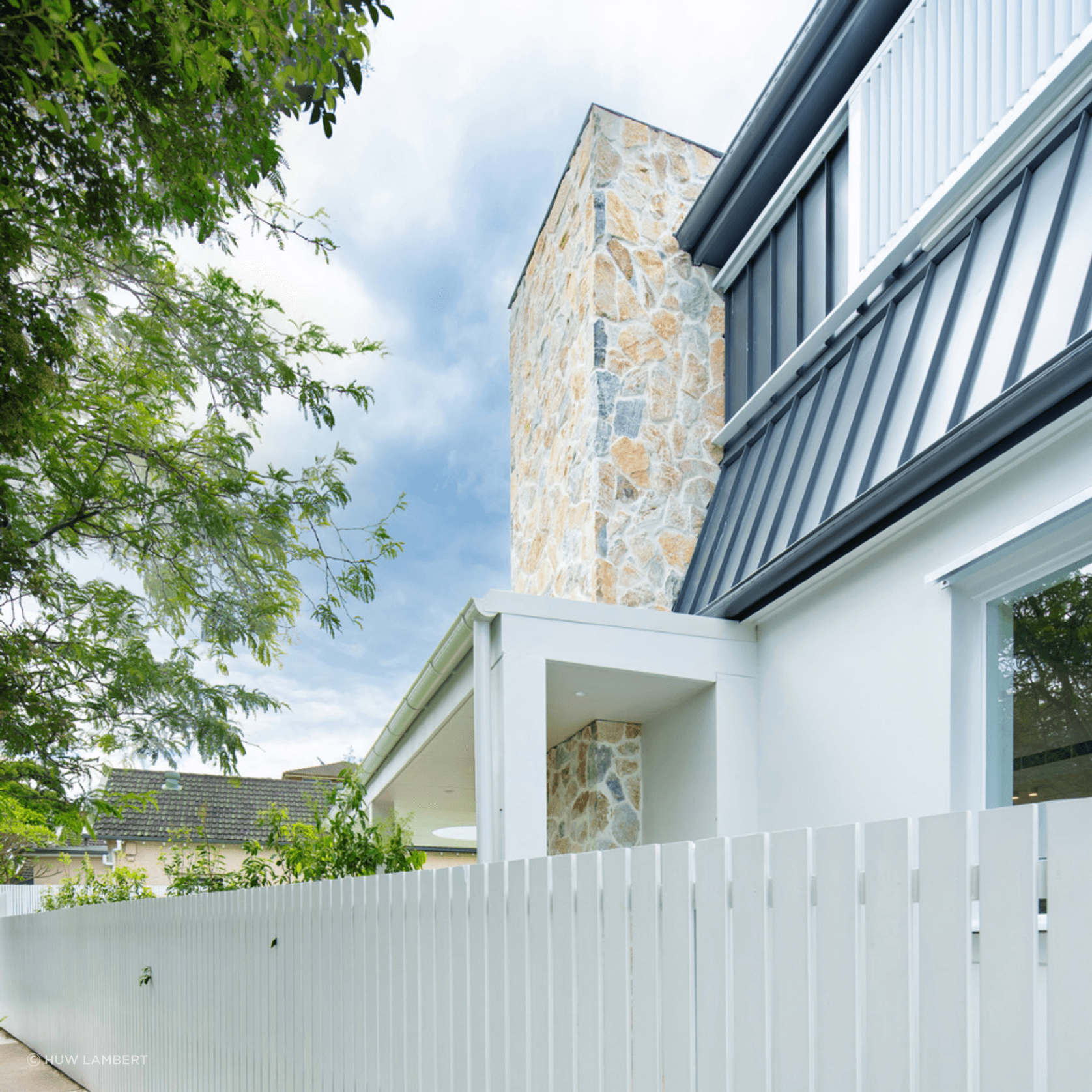 Exterior home facade featuring Summit natural stone wall cladding with white render and charcoal metal roofing.