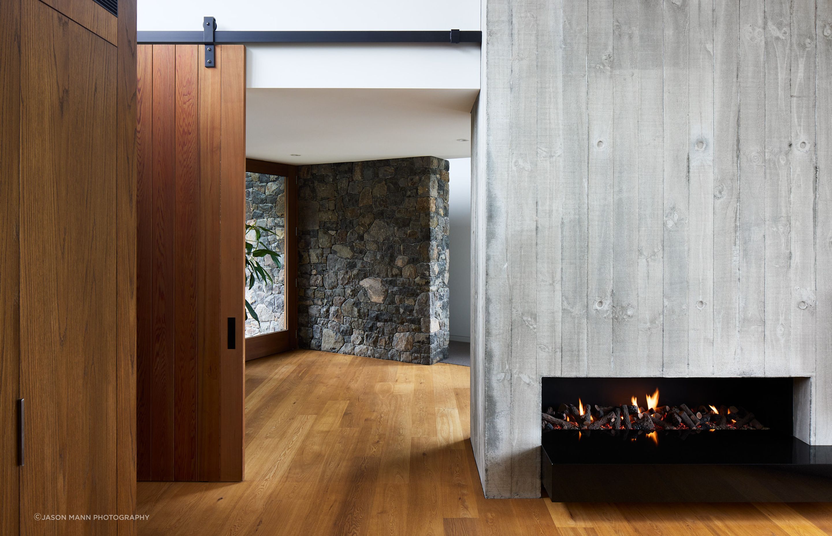 The entrance hall sits at the “knuckle of the two wings”.  Its lower ceiling height feels protective, complemented by warmly toned timber. Locally sourced volcanic stone extends from the exterior into the interior, softening the transition whilst firmly rooting the residence in the Port Hills.