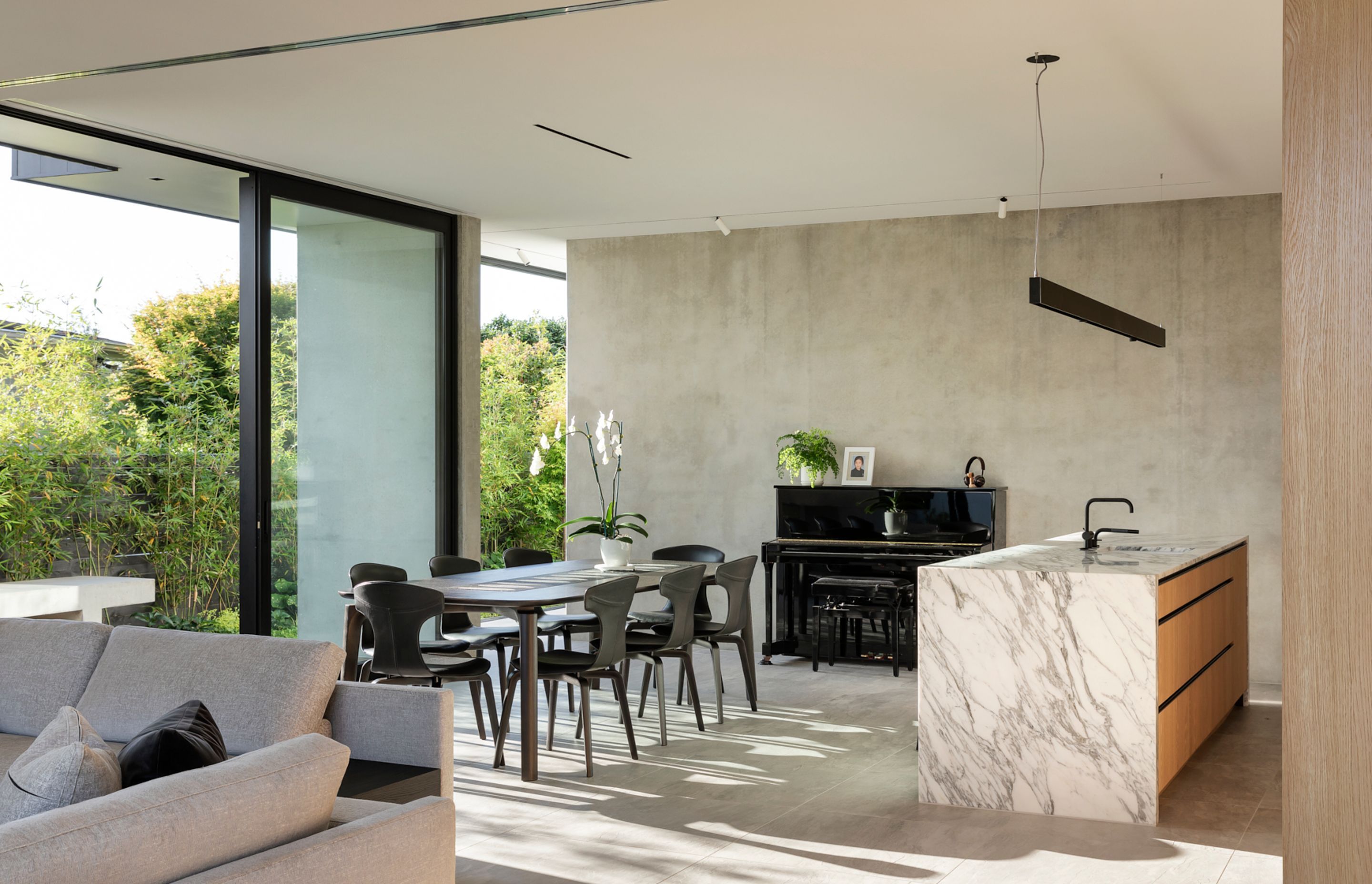 A black piano takes centrestage against a polished concrete wall while the beautiful veining in the marble kitchen island competes with the bamboo shadows on the floor.