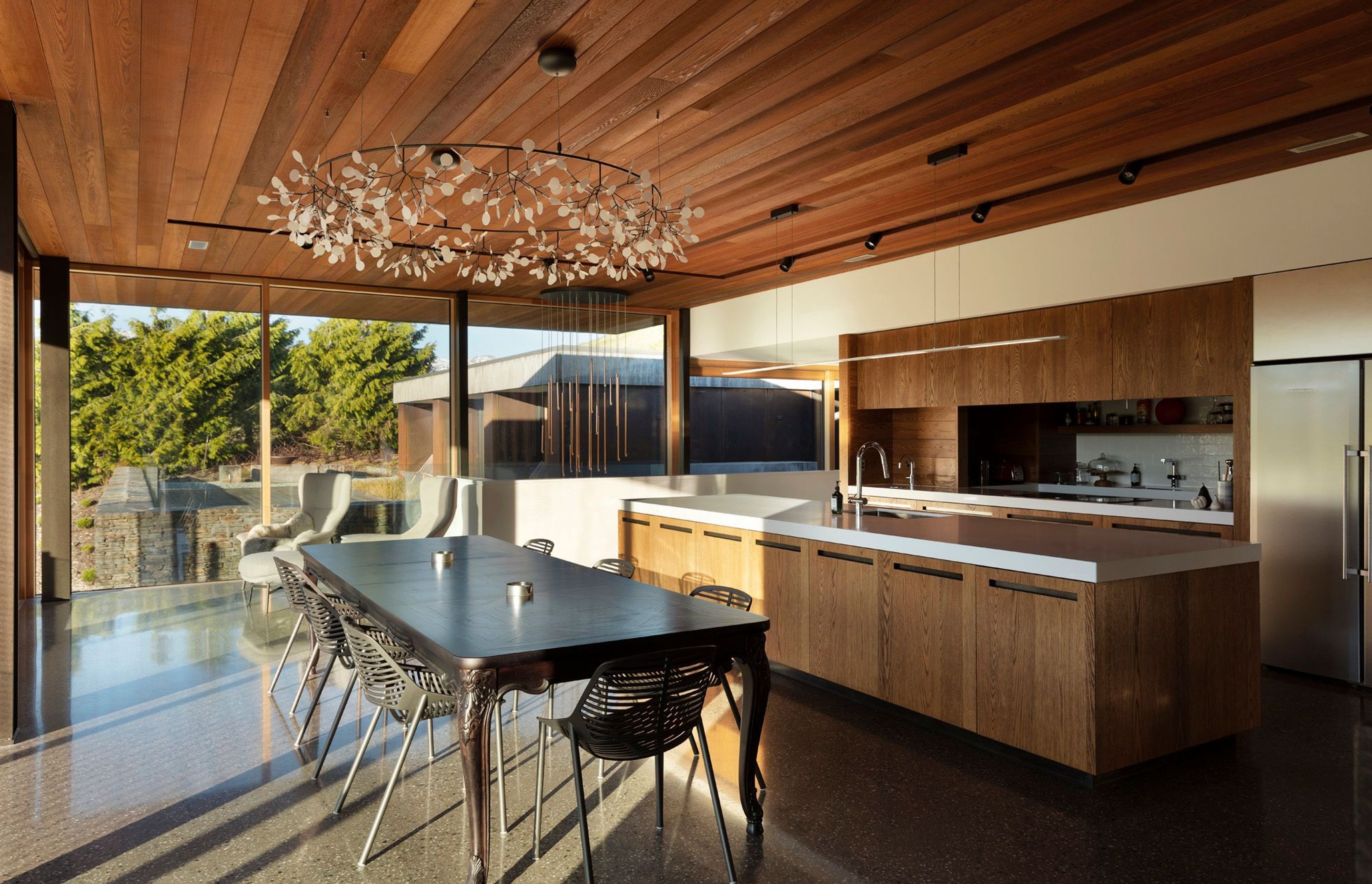 The kitchen and dining area features a cedar-panelled ceiling and oak cabinetry, providing a warm contrast to the polished concrete floor and stainless steel appliances.