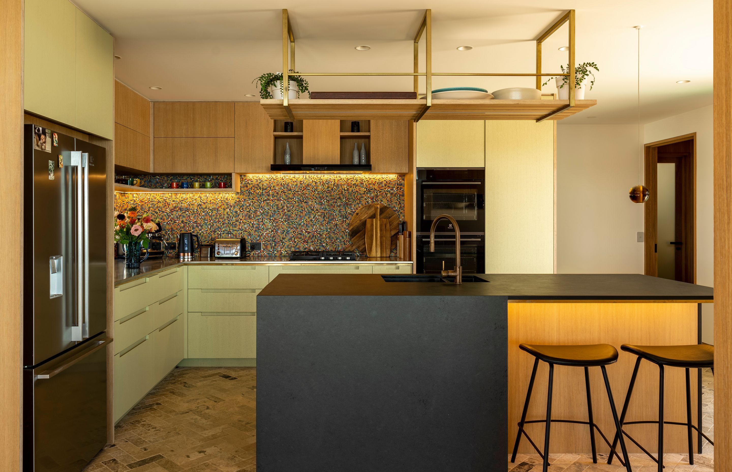 A colourful kitchen splashback and green oak cabinetry feature in the kitchen.