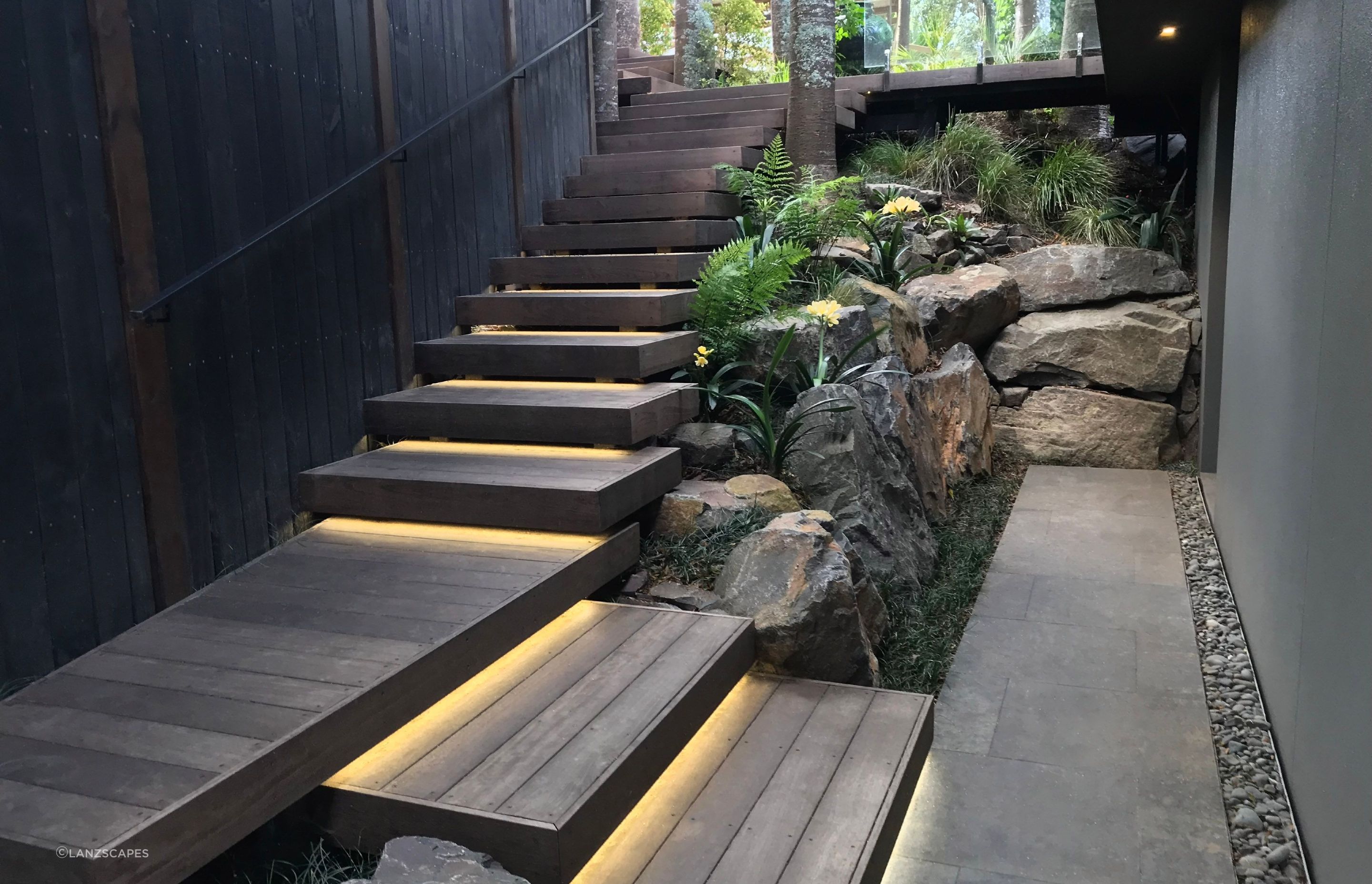 Rock retaining, floating hardwood stairs and stone paving with native/subtropical planting theme.