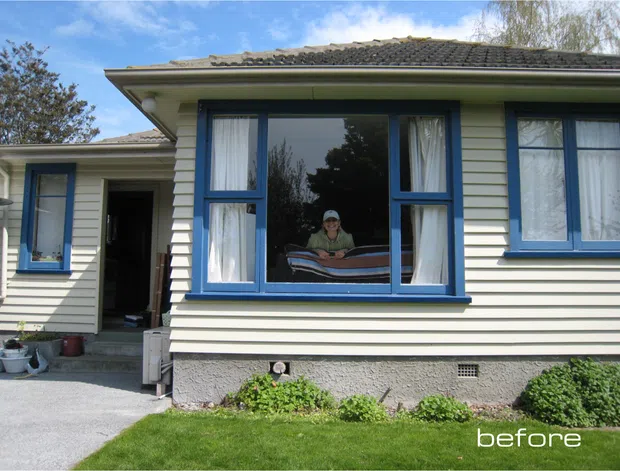 Exterior view of a single-storey weatherboard house with a low-pitched tiled roof, blue-painted timber window frames, a projecting bay window, and a front entry along a paved path. The image is labelled “before” and shows a modest residential facade with lawn and established planting.