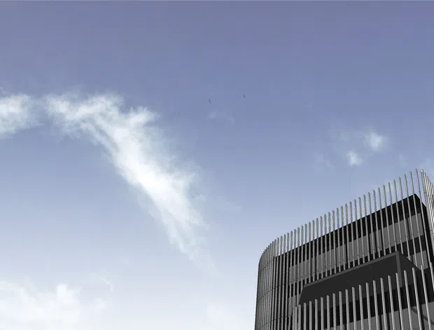 Upward-looking exterior view of a contemporary multi-storey building corner, dominated by a dark facade screened with closely spaced vertical fins and a curved edge. The building occupies the lower-right portion of the frame against an expansive pale blue sky with wispy clouds.