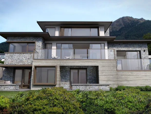 Contemporary multi-level residential house set against a mountainous backdrop. The facade combines pale stacked-stone masonry, horizontal timber-look cladding, broad glazed openings, dark-framed windows, projecting flat roof planes, and multiple terraces or balconies.