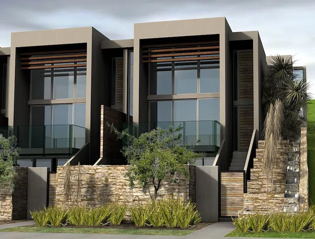 Front exterior view of a contemporary multi-level townhouse development with two prominent dark-rendered volumes, large glazed openings, projecting balconies with clear glass balustrades, horizontal timber screening, and layered natural-stone retaining walls. Low-maintenance landscaped planting and tall sculptural palms frame the facade.