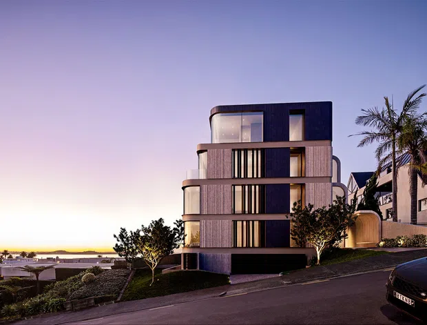 Dusk exterior rendering of a contemporary multi-storey residential building on a sloped suburban site. The building has a rounded, sculptural massing with horizontal floor bands, dark vertical window openings, extensive glazing, and a dark recessed ground level. Landscaping and neighbouring homes are visible, with a distant coastal-looking horizon beyond the site.