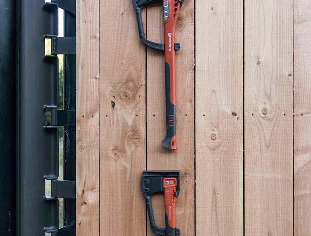 Close-up exterior detail of two red-and-black power tools mounted vertically on a natural timber plank wall beside a dark metal structural frame. The image focuses on the tools and the contrasting wood and metal surfaces.