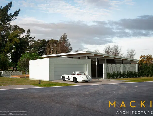 A single-storey modern residence viewed from the street, featuring a broad low-pitched roof, white rendered walls, grey horizontal garage cladding, covered entry, patterned privacy screens, and a white sports car in the driveway. Mature landscaping surrounds the property, with a paved road in the foreground. Architectural practice branding appears at the lower right.