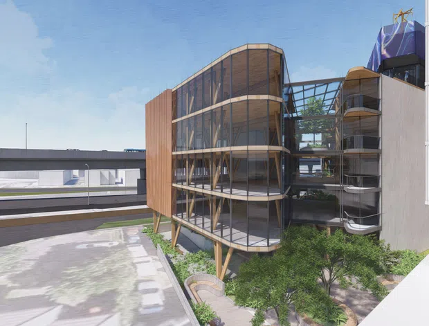 Architectural visualization of a contemporary multi-storey building with a rounded, timber-toned screened facade, extensive floor-to-ceiling glazing, exposed structural framing, and elevated sections above a landscaped courtyard. Adjacent white building volumes and elevated transport or bridge infrastructure are visible in the urban setting.